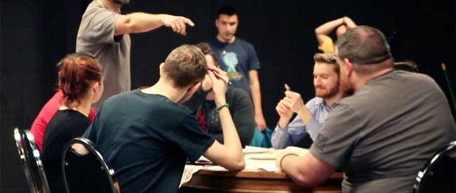 Archer (above, pointing) directing the student actors as they run through a scene around the table.