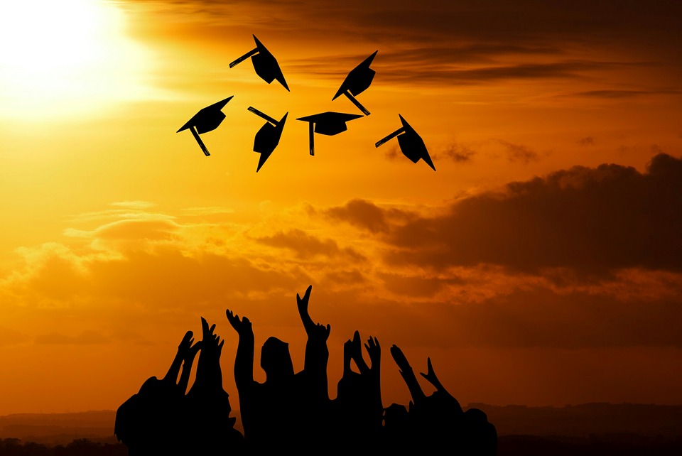 Photo of a group of students tossing their graduation caps into the sunset.