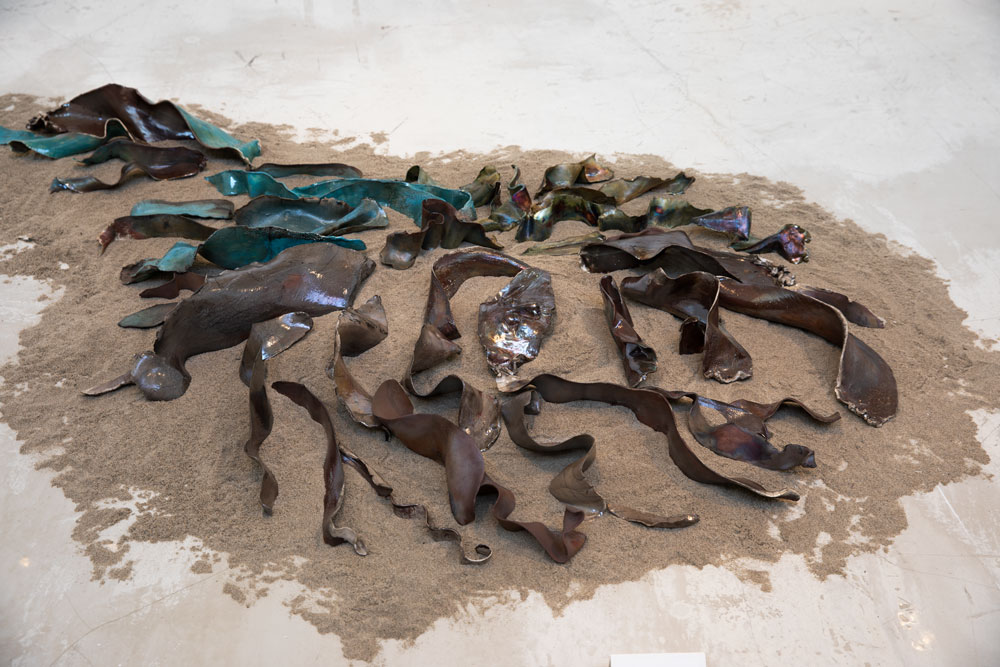 Photograph of Molly Anderson's "Ripple" with unformed pieces of clay laid on sand on the ground.