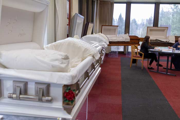 A row of caskets on display with two people at a table discussing arrangements in the distance.