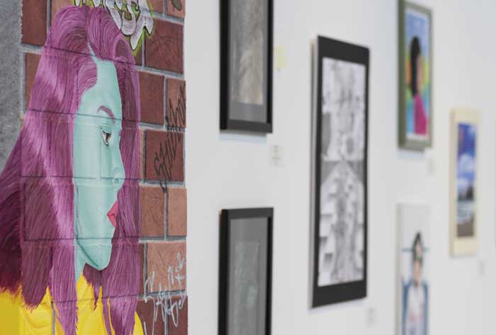 Slanted photo of various art hanging on a wall, a woman painted on a brick wall