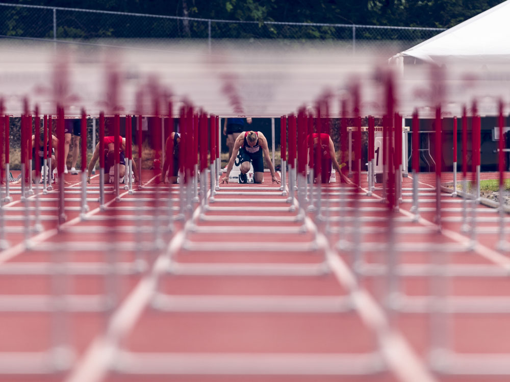 View of hurdler Alex Moore through all of the hurdles as he prepares to take off from blocks