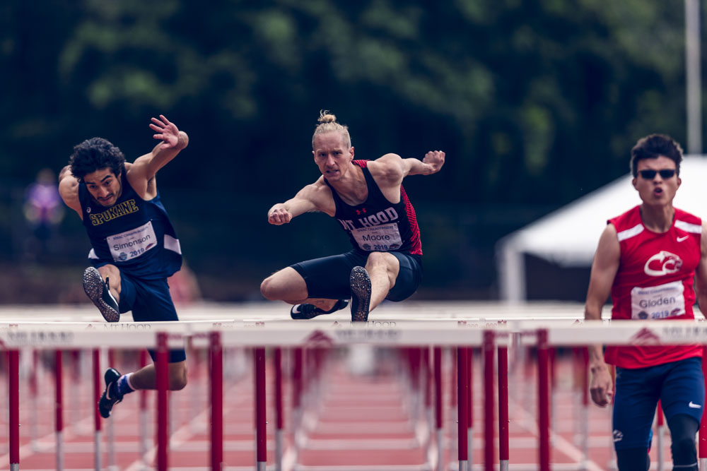 Alex Moore hurdling toward the camera with opponents on left and right