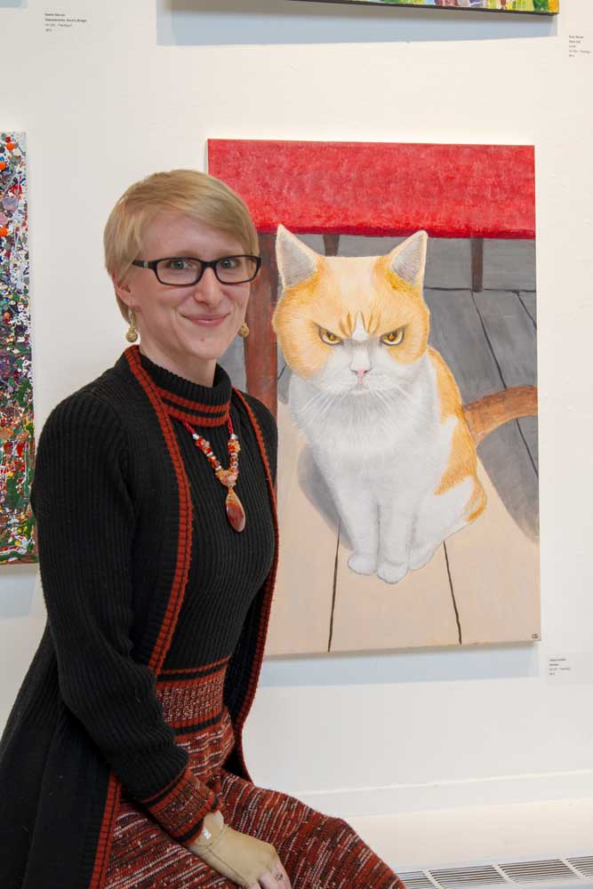 Claire Curtiss sits next to her painting of an orange cat.
