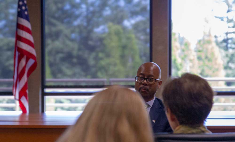 Two heads in foreground facing McQuarters who is facing the camera.