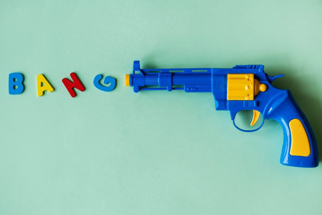 A toy gun laid down with colorful magnet letters spelling the word, "BANG"