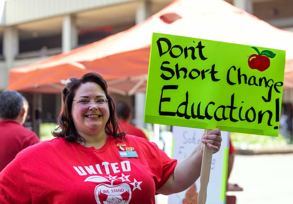 Belnap holding a sign that says, "Don't short change education!" while wearing a red shirt as part of the campaign.